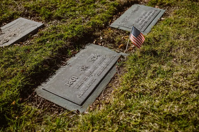 A gravestone adorned with an American flag in a green cemetery, symbolizing honor and remembrance. Deaths today 2027: a dated archive with source links