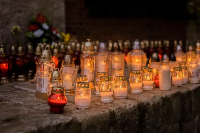 A serene scene of votive candles glowing softly in a cemetery during All Saints' Day. Deaths today timeline: dates, careers and public records